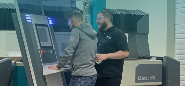 two individuals standing in front of a waterjet table and controller