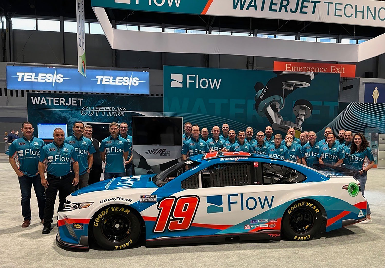 Flow employees standing in tradeshow booth with the #19 Flow Nascar