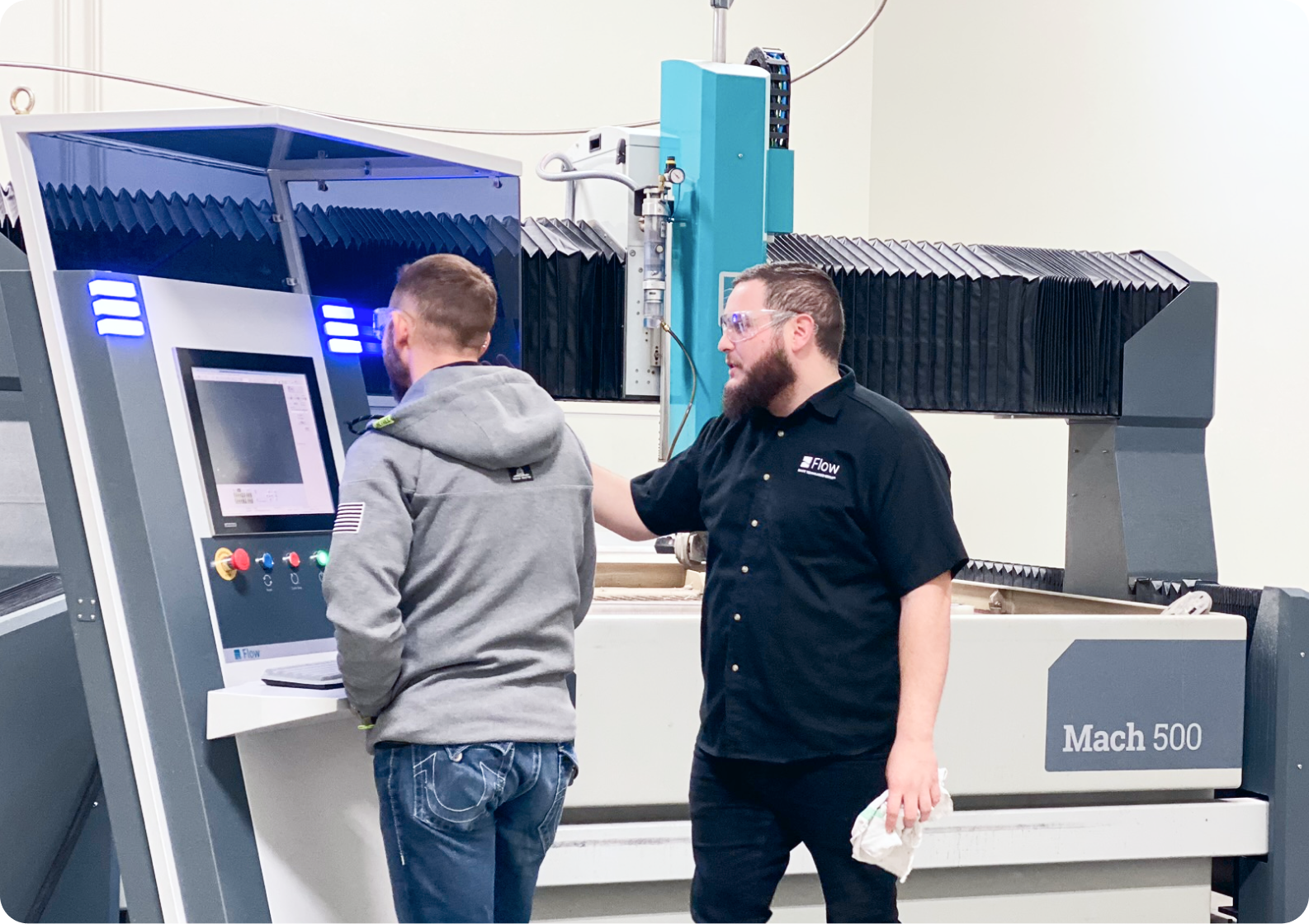 Flow employees in front of a Mach 500 waterjet working on a roll around control
