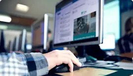 someone sitting at a computer with their hand on the mouse with a blurry monitor in the background