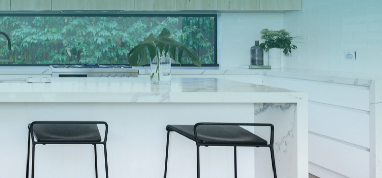 Black stools seated in front of a white stone with grey marbling cut into a waterfall island in a kitchen